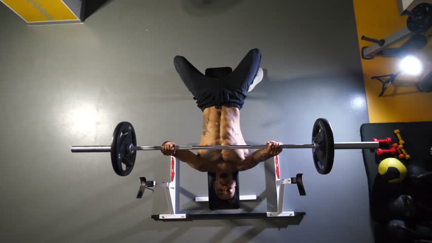 Muscular african man doing bench press workout with a barbell at sport club. Young afro american sportsman doing weightlifting exercises at modern gym. Healthy and active lifestyle concept. Top view