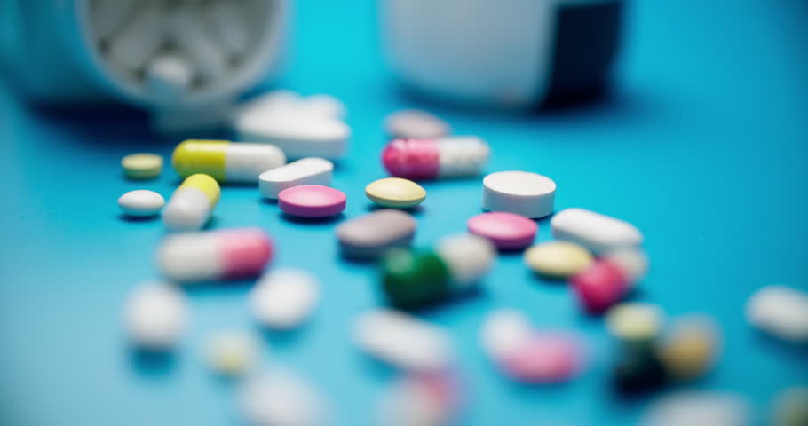 Slider motion close-up of assorted colorful pills and capsules on turquoise background. Low-angle shot with shallow depth of field highlighting vibrant textures.