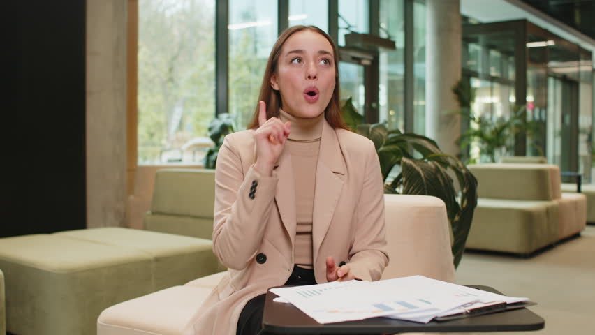 Eureka. Thoughtful clever inspired Caucasian woman make gesture raises finger came up with creative plan feels excited with good idea inspiration motivation question in hotel lobby. Girl sits in hall.