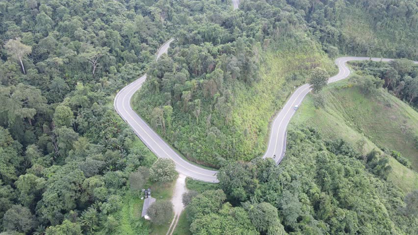 Aerial View of Curved Road Through Green Fields and Hills in Countryside Landscape