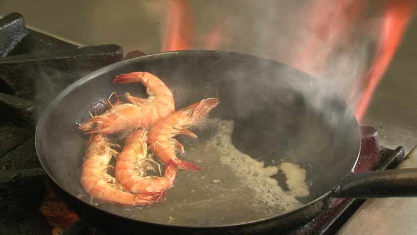 Hokianga, New Zealand, April 2013. Chef prepares prawns in pan over gas hob,