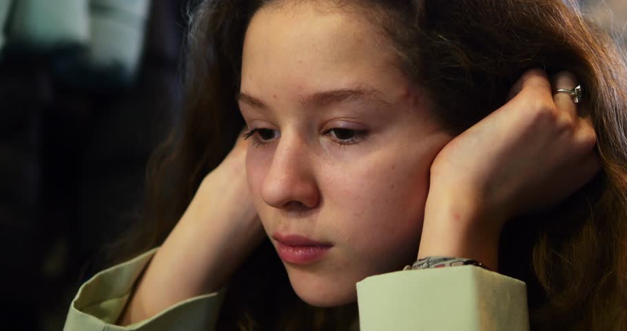 Sad teenage girl deeps in thoughts with melancholic and contemplative expression. Young lady hands rest on head suggesting state of worry and concern