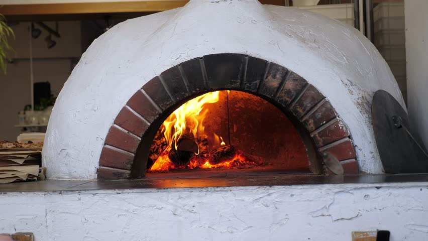 A traditional pizza oven with a spatula. The cook puts the pizza to bake in the oven with fire using a spatula. The pizza making process. There's wood burning in the oven. - Powered by Shutterstock - Get 15% off with code: PIKWIZARD15