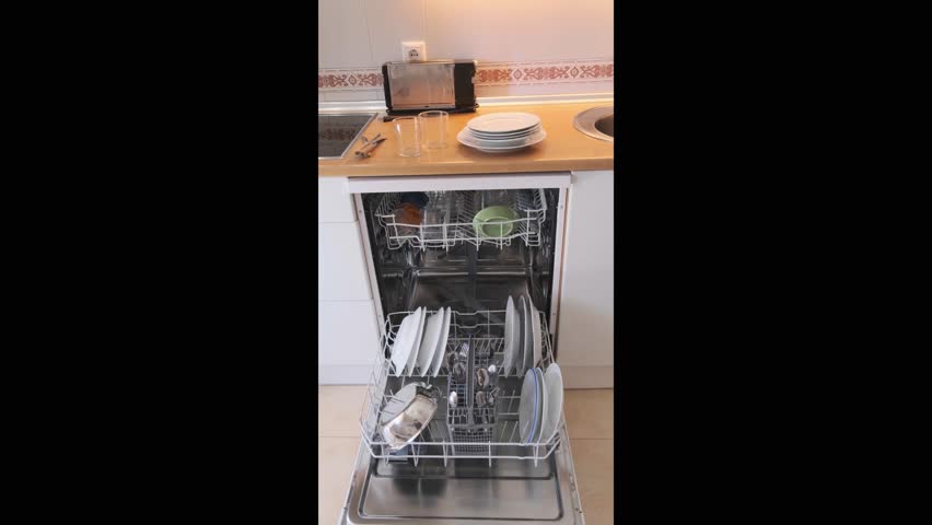 A man collecting clean cutlery from inside an open dishwasher in a modern kitchen. Vertical format