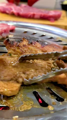 Close-up of meat grilling on a BBQ in a Bangkok restaurant. Tongs turn the sizzling meat over a hot grill