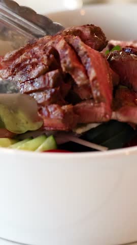 Slices of grilled beef are artfully arranged in a salad bowl under warm, inviting lighting