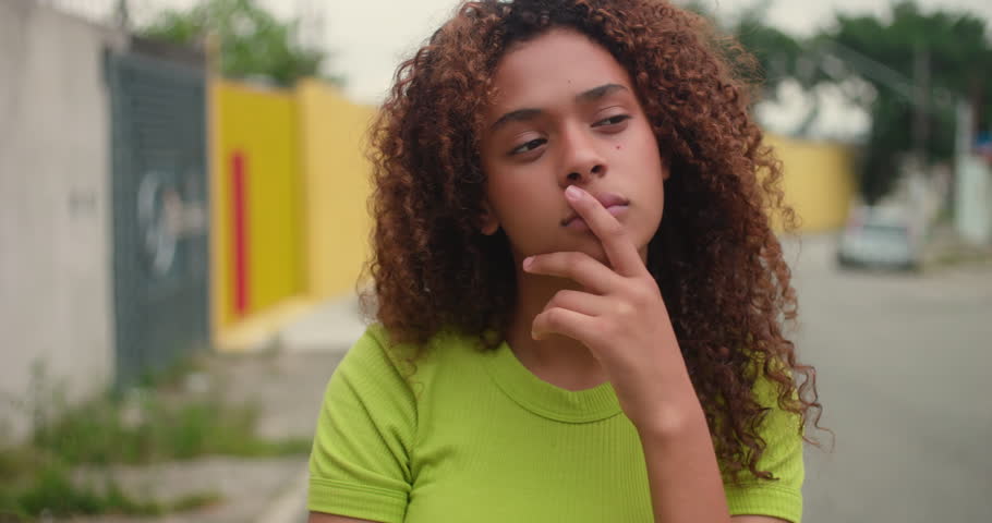 Teenage girl standing alone in the street, hand resting on chin, looking up in deep thought, introspective moment, personal reflection, decision-making, and contemplation
