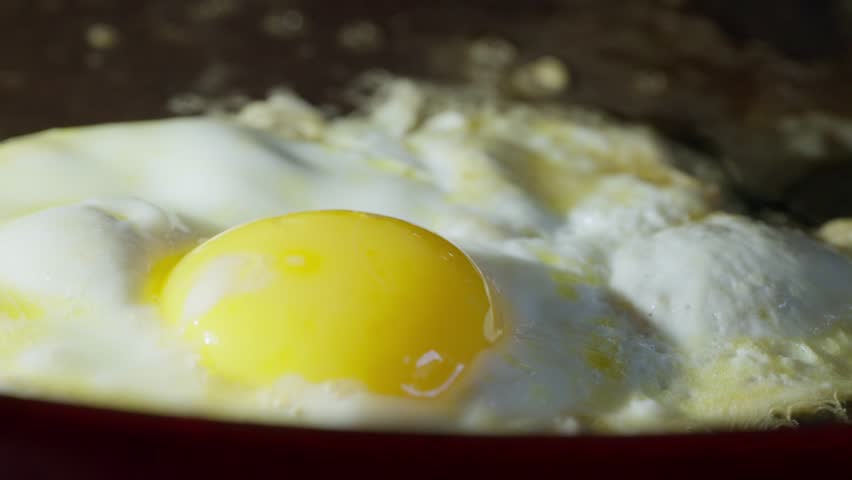 Fish slice lifting fried egg to prevent burning on hot frying pan, macro closeup