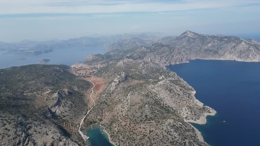 A yacht rests in a protected lagoon surrounded by rocks, reefs, and golden coastline.