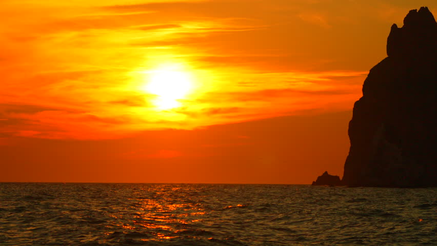 Sunset Rocks Ocean: Dramatic fiery sunset illuminates coastal rock formations at ocean during golden hour.