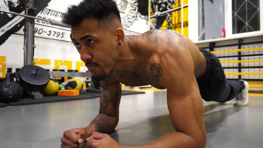 Young sportsman doing a plank at sport club. Sporty man strengthens his abdominal muscles at modern gym. Athletic guy exercising in fitness centre. Sportive lifestyle