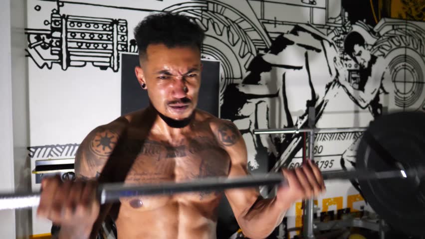 Muscular sportsman performing intense barbell curl exercises at modern gym. Athletic guy doing hard workout at sport club. Sporty man training at fitness centre. Close up