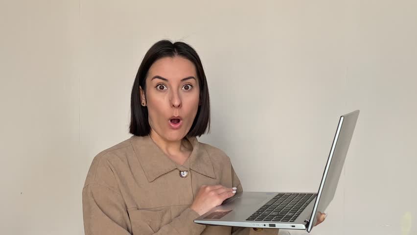 Shocked young woman holding laptop shock mouth open looking at camera disbelief amazed unexpected indoor studio portrait isolated girl online reaction technology bad news error disbelief business