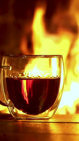 Steaming tea in double-walled glasses glows warmly by the blazing fireplace. Vertical footage