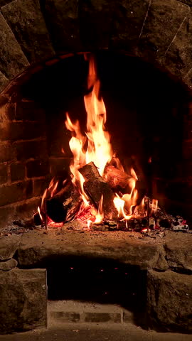 Vertical video of Cozy Fireplace with Burning Logs, A warm fire blazes in a rustic stone fireplace, with glowing embers and vertical flames.