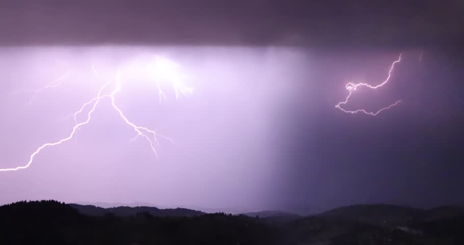 Lightning storm in the night sky at mountain. Multiple lightnings and thunders illuminate night sky and hills