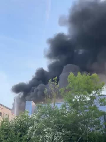 An old college building burning down, black smoke making the bright sunny day look so miserable and dull. 