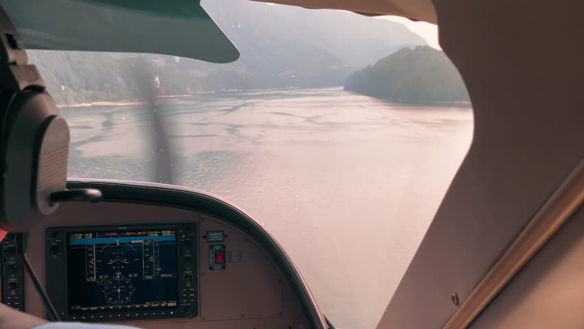 Cockpit view of small aircraft flying over calm mountain lake, digital instruments and scenic landscape ahead