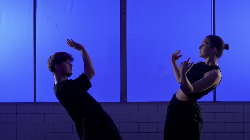Two dancers perform a contemporary dance routine with expressive movements against a striking blue background. Slow motion