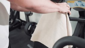 Young man drapes sports towel over rubber chair backrest before workout in modern gym with sleek weight machine and bright interior lighting preparing equipment for fitness routine session - Powered by Shutterstock - Get 15% off with code: PIKWIZARD15