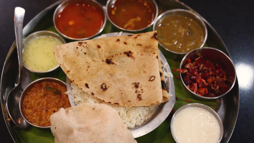 Indian vegetarian platter Thali meals. Having paneer butter masala dal makhani flat bread or naan and rice served in a steel plate and banana leaf Tamil Nadu Bangalore Karnataka India.