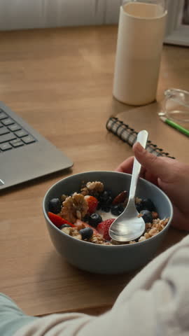 Vertical shot of unrecognizable woman eating granola with fresh berries while sitting at table