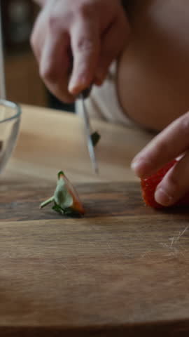 Vertical shot of unrecognizable woman cutting fresh strawberry with knife in kitchen
