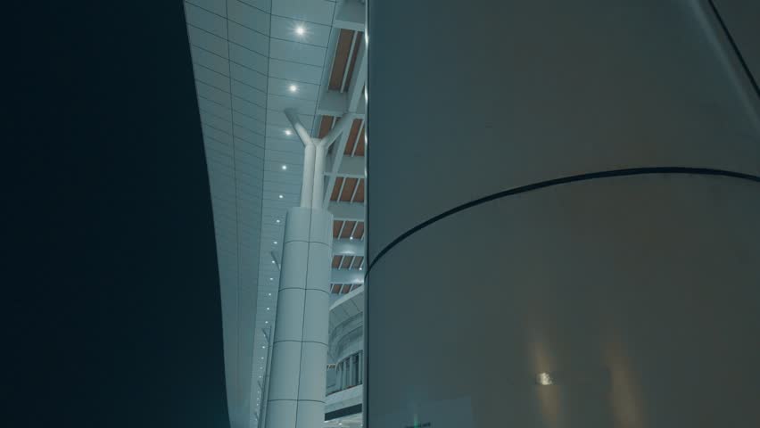 A modern architectural structure featuring sleek lines and illuminated columns at night. The design showcases a blend of glass and metal elements, emphasizing a contemporary aesthetic.