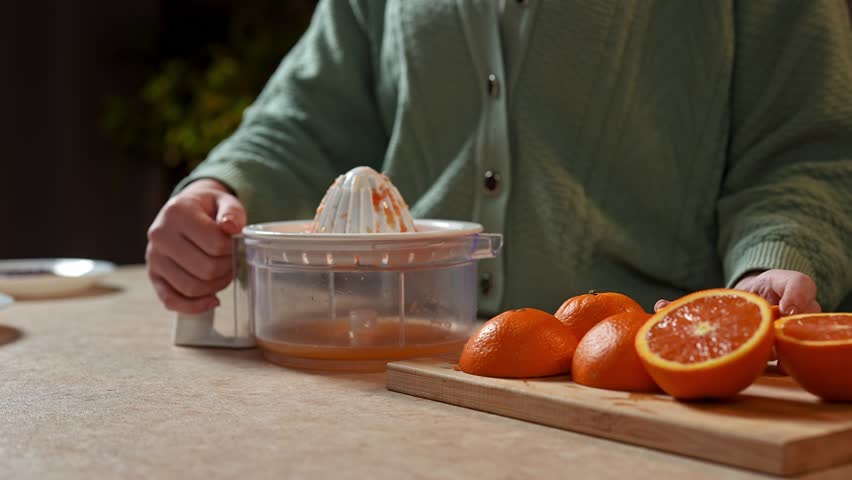 Healthy eating concept. Woman at the table in the kitchen preparing healthy vegetable salad for dinner, woman making orange juice, squeezing oranges with hand squeezer. Slow motion