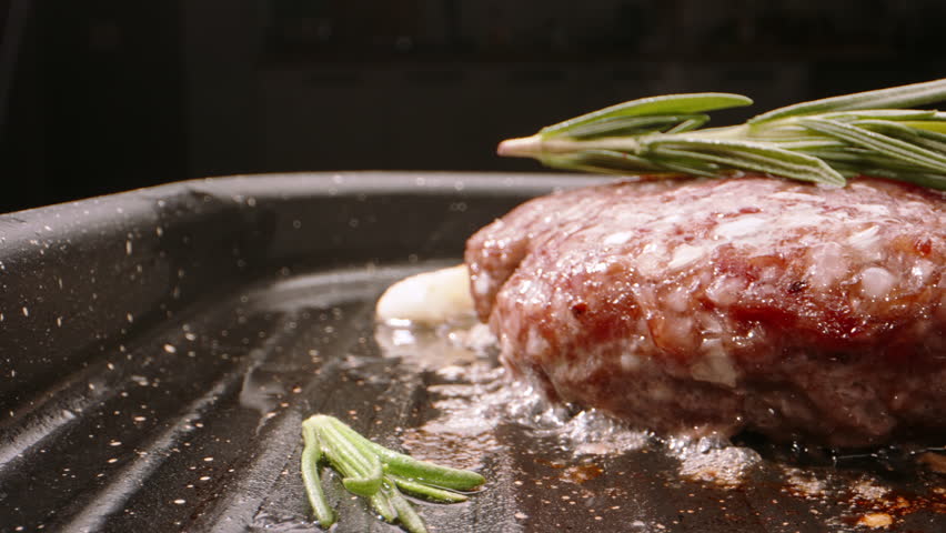 Pork cutlet for burger fried in frying pan. Perfect pork patty is pan-fried with rosemary sprigs, garlic and cherry tomatoes. Cinematic video for burger advertisement. Delicious and juicy pork cutlets