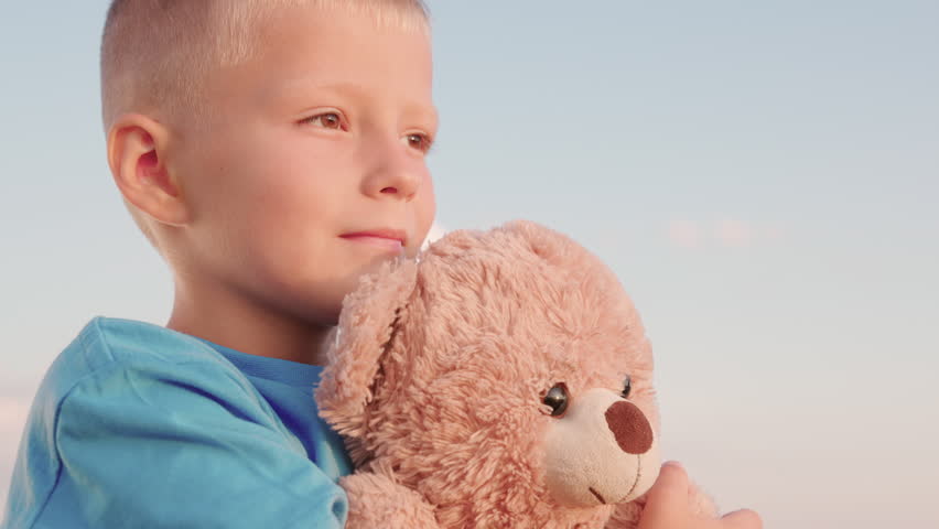 Child plays with Teddy bear. Kid plays with toy, Plush toy in hands of boy, child in summer park. Cute child baby boy hugs his favorite soft teddy bear on playground. Portrait of child with bear toy