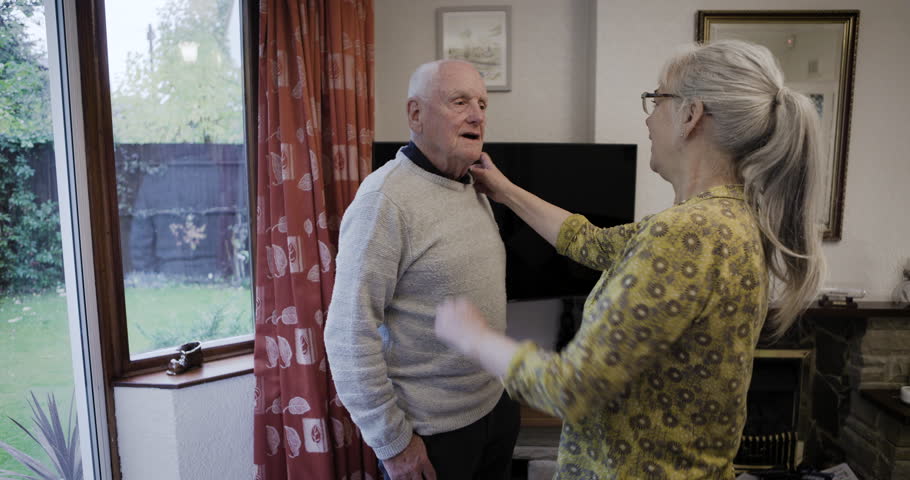 Senior couple, man and woman with help for dress up with clothes, homecare support and care in home. Elderly people, helping hand and shirt collar to start morning together for happiness in house