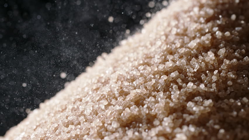 Brown cane sugar is poured into pile, half pile. Close up slow motion. Cutting down on sugar is vital to combat rising threat of obesity, diabetes, and other health concerns. Nutrition diet modern