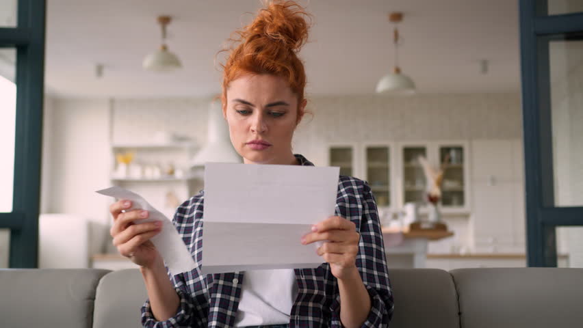 Caucasian woman serious homeowner girl female at home couch reading letter paper notification debt trouble check payments bills analyze expenses budget money finances loan credit bank mortgage problem