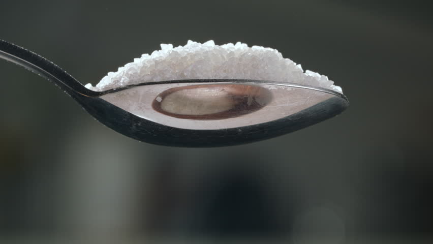 Spoon of white sugar. Close up slow motion blurred background. Sugar quietly infiltrates our diets. Increased risk for chronic diseases like diabetes and heart disease. Overuse of sugar in products