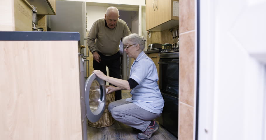 Helping, cleaning and senior couple doing laundry, loading clothes and housework in washing machine. Working, help and elderly man and woman talking and sorting clothing for chores and housekeeping