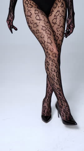 Unrecognized woman's legs in black lace stockings and black high-heeled shoes. Model walks and turns by the white floor in studio. Vertical video.