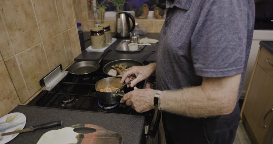 Old man cooking food at stove, kitchen and lunch meal at home. Senior male prepare dinner in pan for fresh, hot and healthy recipe in retirement, hungry pensioner and heating ingredients for eating