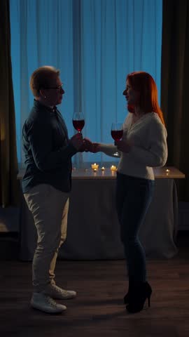 A silhouette of a couple enjoying a romantic evening at home, sharing glasses of red wine and creating a warm, intimate atmosphere. Slow motion. Vertical Video.
