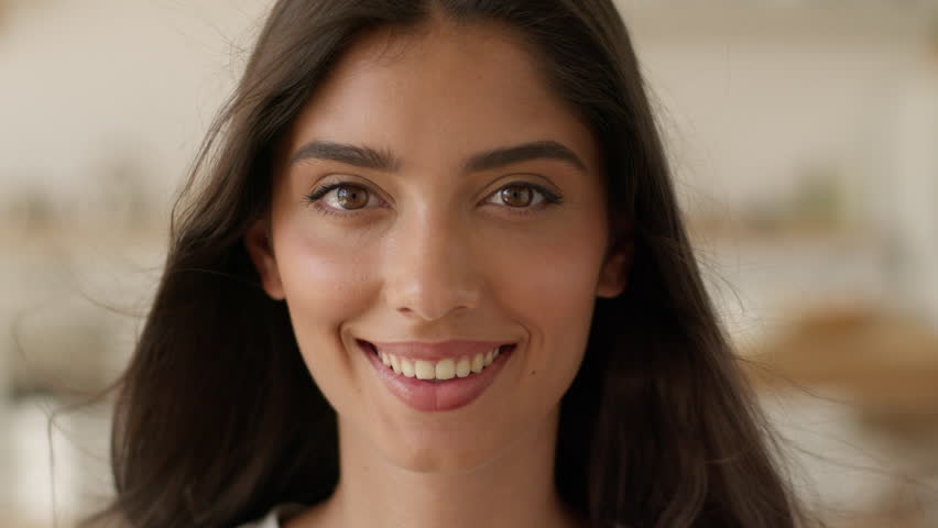 Arabian millennial woman Indian girl ethnic looking at camera look smiling healthy toothy smile dentistry positive female satisfied glad portrait at home apartment blowing flying hair air conditioner