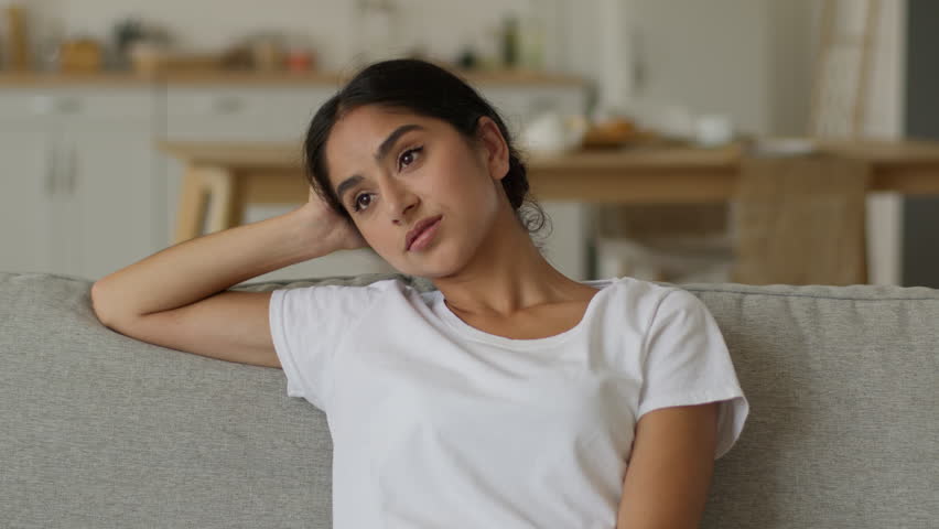 Stressed Arabian woman Indian girl tired frustrated lady fatigued overworked female at home sitting on couch cozy comfortable sofa relaxing resting health problem relaxed pause break air conditioner