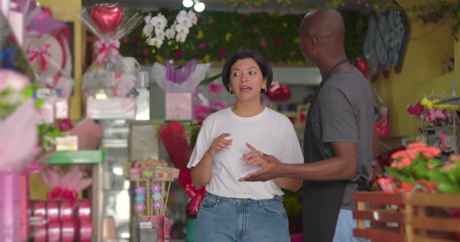 Man giving woman blue orchid bouquet inside flower shop, florist presenting fresh flowers to customer in vibrant store full of floral arrangements and gifts