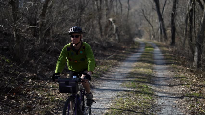 A mature woman enjoys biking on the scenic rail trail next to the Potomac, surrounded by early spring vegetation in Western Maryland.