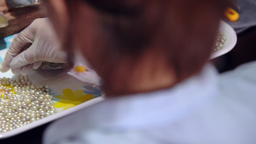 In a Vietnamese pearl farm, a woman hand touches a collection of beautiful and precious pearls on the table. The rich tradition of cultured pearl farming in Vietnam and the natural beauty sea gems.