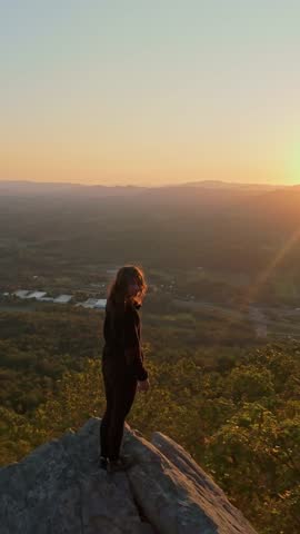 Person standing at edge of a rocky outcrop on Buffalo Mountain, Tennessee, gazing over vast forested valley during golden hour, evoking sense of freedom, reflection, and connection with nature