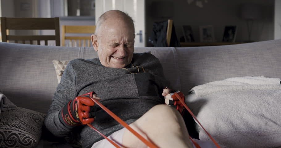 Senior man, legs rehabilitation and band for fitness, healing and stretching at home in England. Wellness, health or physiotherapy of old man doing orthopedic exercise for arthritis or osteoporosis