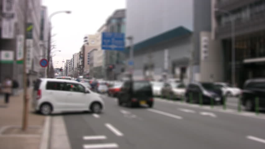 Movement of cars and pedestrians on a city street. The focus at the far end of