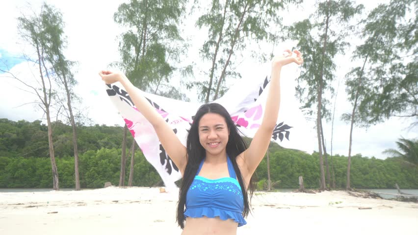 A woman with long hair is standing on a beach. The sky is cloudy and the ocean is in the background