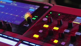 A close-up of a digital mixer console featuring vibrant illuminated buttons and dials. The interface displays waveform monitors and various controls for audio mixing - Powered by Shutterstock - Get 15% off with code: PIKWIZARD15