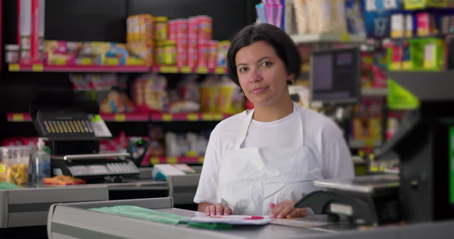 Supermarket worker smiling behind checkout counter, casual indoor grocery store environment with colorful shelves and cheerful atmosphere